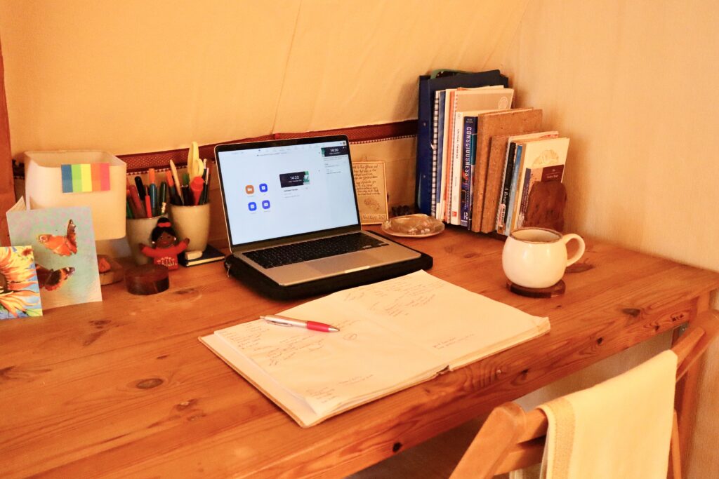 Laptop open on a wooden desk with a notebook, mug, and stationery, set up for listening to therapy podcasts
