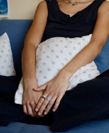 Woman sitting on a blue sofa with hands clasped, holding a patterned pillow, during a therapy session