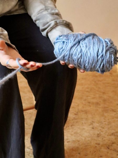 Person holding a large ball of blue yarn, unwinding a strand between their fingers