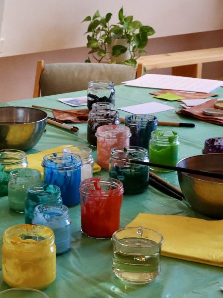 Table covered with jars of colorful paint, paintbrushes, and mixing bowls set up for an expressive art therapy session